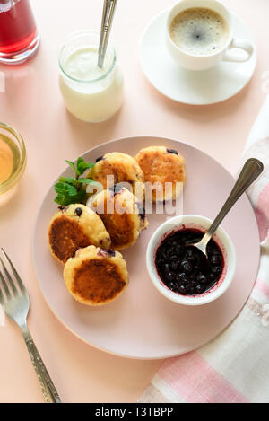 Cottage cheese pancakes with blueberry, honey, jam and coffee. Ukrainian syrniki, cottage cheese fritters or pancakes on pink wooden background. Healt Stock Photo