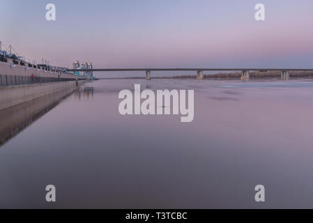 Beautiful gentle pink sunset on a fast river with a bridge and ice drift shot on a long exposure Stock Photo