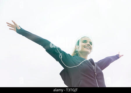Female young athlete stretching her arms  while listening to music outdoors Stock Photo