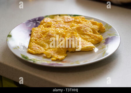 Plate with delicious fluffy omlette with cheese interior and very well roasted sits on a kitchen front. Organic homemade breakfast for champions Stock Photo