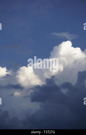 layered clouds, fluffy white and dark grey, in front of blue sky Stock Photo