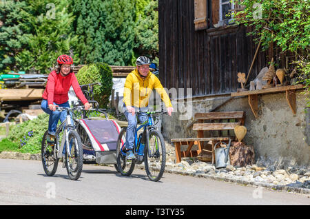 Young family with trailer cycling in rural village Stock Photo