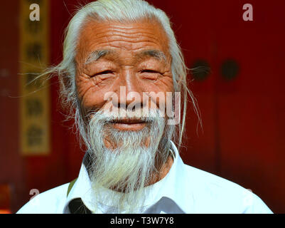 Old Chinese man with long white Chinese beard smiles for the camera in front of Kunming's Buddhist Yuantong Temple. Stock Photo