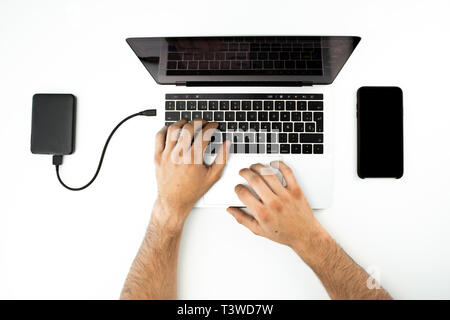 Businessman working with his laptop computer and his smartphone on a white table. Modern workplace. External hard drive connected to the computer. Stock Photo