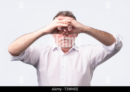 senior man holding his hands at his eyes as if looking through binoculars Stock Photo