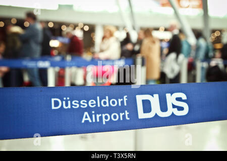 12 April 2019, North Rhine-Westphalia, Düsseldorf: Passengers are standing behind a barrier tape with the inscription 'Düsseldorf Airport DUS'. On Saturday the Easter holidays start in North Rhine-Westphalia. Photo: David Young/dpa Stock Photo