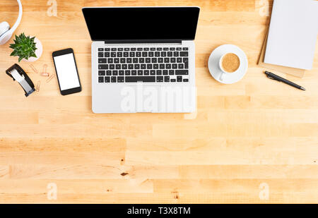 Modern laptop computer. Top view of wooden office desk with laptop computer, smartphone, notebook, headphone, plant and cup of coffee. Modern office.  Stock Photo