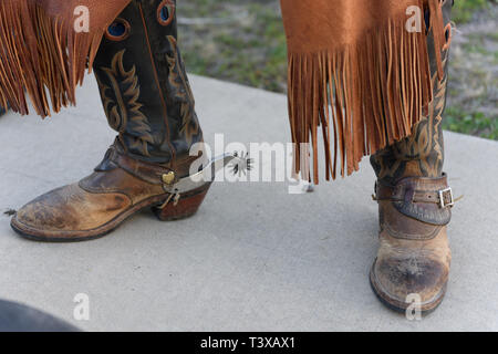 Old worn cowboy boots with spurs on an old cowboy wearing leather chaps. Stock Photo