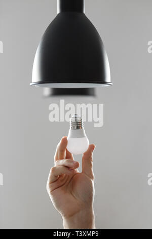 Changing the bulb for led bulb in floor lamp in black colour. On light gray background. Stock Photo