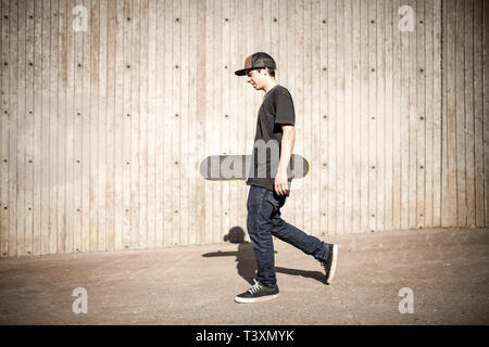 Caucasian man carrying skateboard near wooden wall Stock Photo