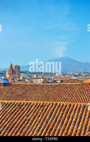 Roofs of the old town of Catania and Mount Etna volcano with smoke, Sicily, Italy Stock Photo