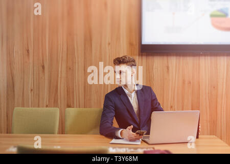 A stylish young man in a jacket and shirt sits at the desk with his colleagues and works with documents at office Stock Photo