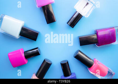 Bottles of nail polish. A group of bright nail polishes on a blue background. With empty space in the middle. View from above Stock Photo