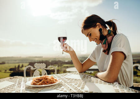 Close up of a woman dining out sitting at a restaurant table. Side view of a smiling woman sitting at the table looking down with a glass of red wine Stock Photo