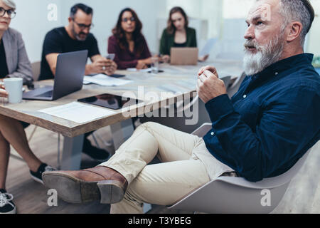 Senior businessman sitting at table with colleagues looking at presentation. Business people paying attention to the presentation. Stock Photo