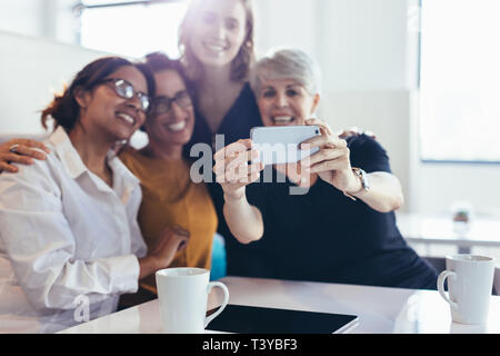 Group of businesswomen taking selfie. Female business professionals taking selfie with smartphone during break in office. Stock Photo
