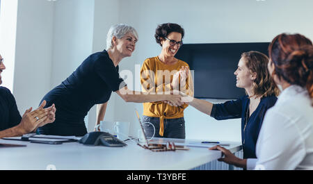 Businesswomen shaking hands and smiling during a business meeting with team clapping hands. Team congratulating and appreciating the performance of a  Stock Photo