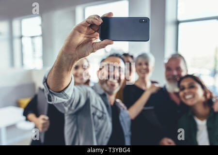 Business people taking selfie of in the office. Business team taking selfie together at startup, with focus on mobile phone. Stock Photo