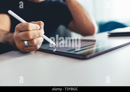 Close up of businessman working on digital tablet with a digitized pen. Man sitting at table and working in office, focus on tablet pc and digitized p Stock Photo