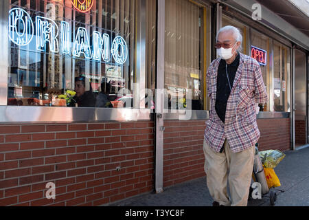 An elderly Asian man walking on Roosevelt Ave in Jackson Heights while wearing a face mask and being attached to an oxygen tank. In Queens, New York. Stock Photo