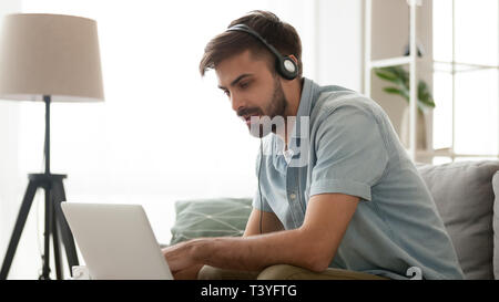 Serious focused man wearing headphones using laptop at home Stock Photo