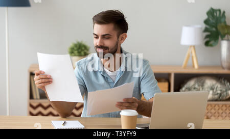 Satisfied man reading paper documents, working with laptop Stock Photo