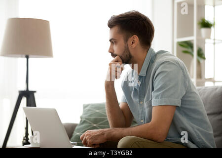 Thoughtful serious man sitting with laptop at home, making decision Stock Photo