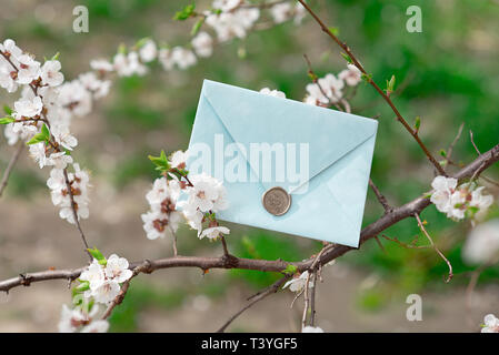 Blue invitation envelope with a wax seal, a gift certificate, a postcard, a wedding invitation card on the background of blooming flowers Stock Photo