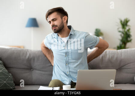 Tired frustrated man suffering from pain, massaging back Stock Photo