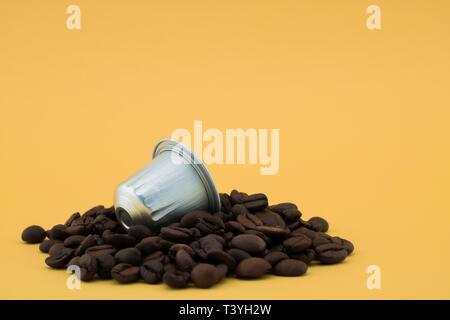 Coffee capsule or coffee pod on coffee beans, yellow background. Capsules for coffee machine. Stock Photo