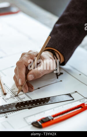 Architect in bracelet. Close up of architect wearing dark jacket and black bracelet making some sketches Stock Photo