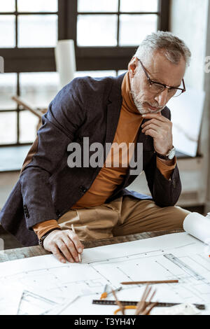 Challenging task. Grey-haired interior designer feeling thoughtful having very challenging task Stock Photo