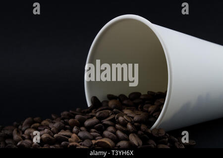 Take-out coffee cup with spilled coffee beans, black background. Roasted coffee beans. Stock Photo