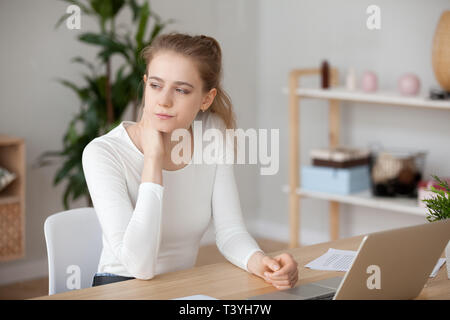 Thoughtful woman sitting in front of laptop, lost in thoughts Stock Photo