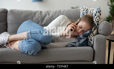 Frustrated woman lying on couch, talk on phone, hearing bad news Stock Photo