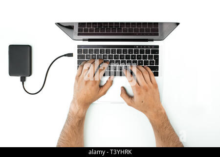 Overhead view of the hands of a person using his laptop on a white table. Business person working in his office. External hard drive connected to the  Stock Photo
