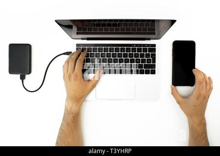 Businessman working with his laptop computer and his smartphone on a white table. Modern workplace. External hard drive connected to the computer. Stock Photo
