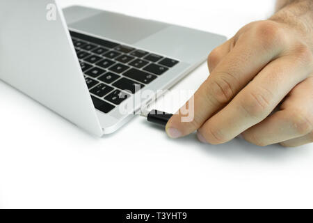 Hand of a person connecting an external hard drive to his laptop on a white table. Modern workplace. Stock Photo