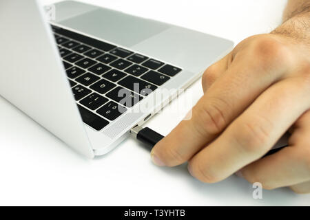 Person connecting an external hard drive to his laptop on a white table. External disk with USB-C input. Modern workplace Stock Photo