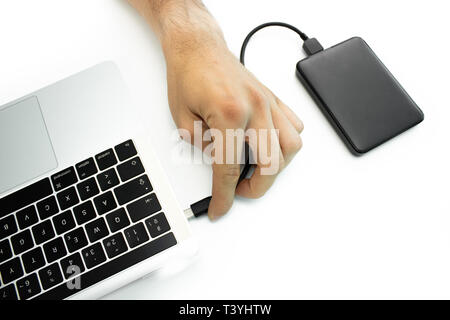Hand of a person connecting an external hard drive to his laptop on a white table. Modern workplace. Stock Photo