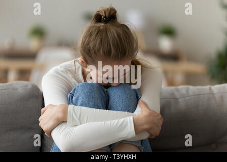 Upset frustrated woman sitting on couch, embrace knees, having problem Stock Photo