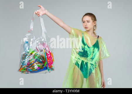 Plastic things. Fair-haired model in plastic clothes holding transparent bag with plastic things in her hand Stock Photo