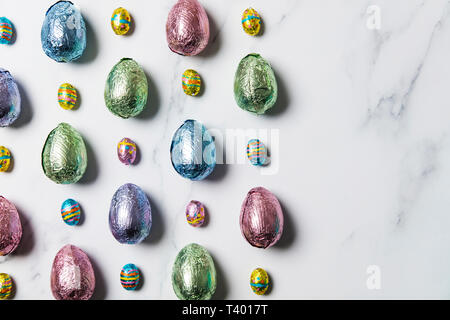 Easter egg chocolate treats wrapped in shiny coloured foil on  marble background Stock Photo