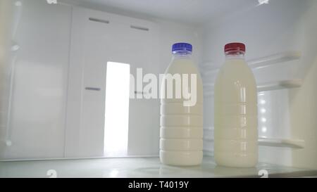 Two bottles of milk in the fridge. a bottle of milk in the fridge. Two bottles of milk in the refrigerator. A bottle of milk with a blue lid. Bottle Stock Photo