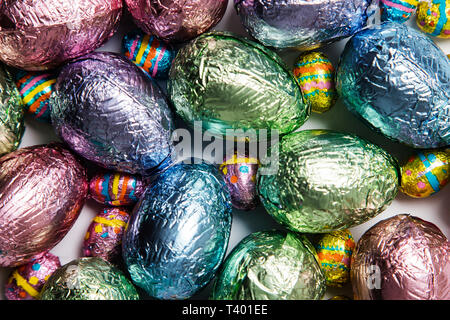 Easter egg chocolate treats wrapped in shiny coloured foil on  marble background Stock Photo
