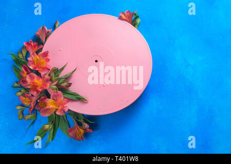 Pink vinyl record with flowers. Color blocking flat lay concept. Musical floral still life on a blue background with copy space Stock Photo