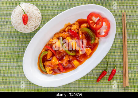 Vietnamese sweet and sour chicken with pineapple and capsicum served with rice. Wooden chopsticks and fresh lime on the side. Top view. Stock Photo