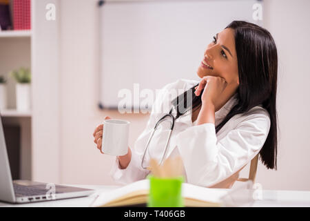 Young doctor is drinking coffee in her office. Stock Photo
