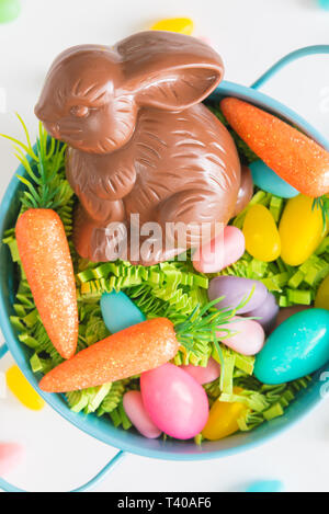 Close-up of chocolate Easter bunny in Easter basket with mini carrots and candy eggs on white background Stock Photo
