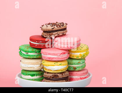 Close up on Macaron cookies in various spring colors stacked on a white plate on pink background. Popular French treat. Stock Photo